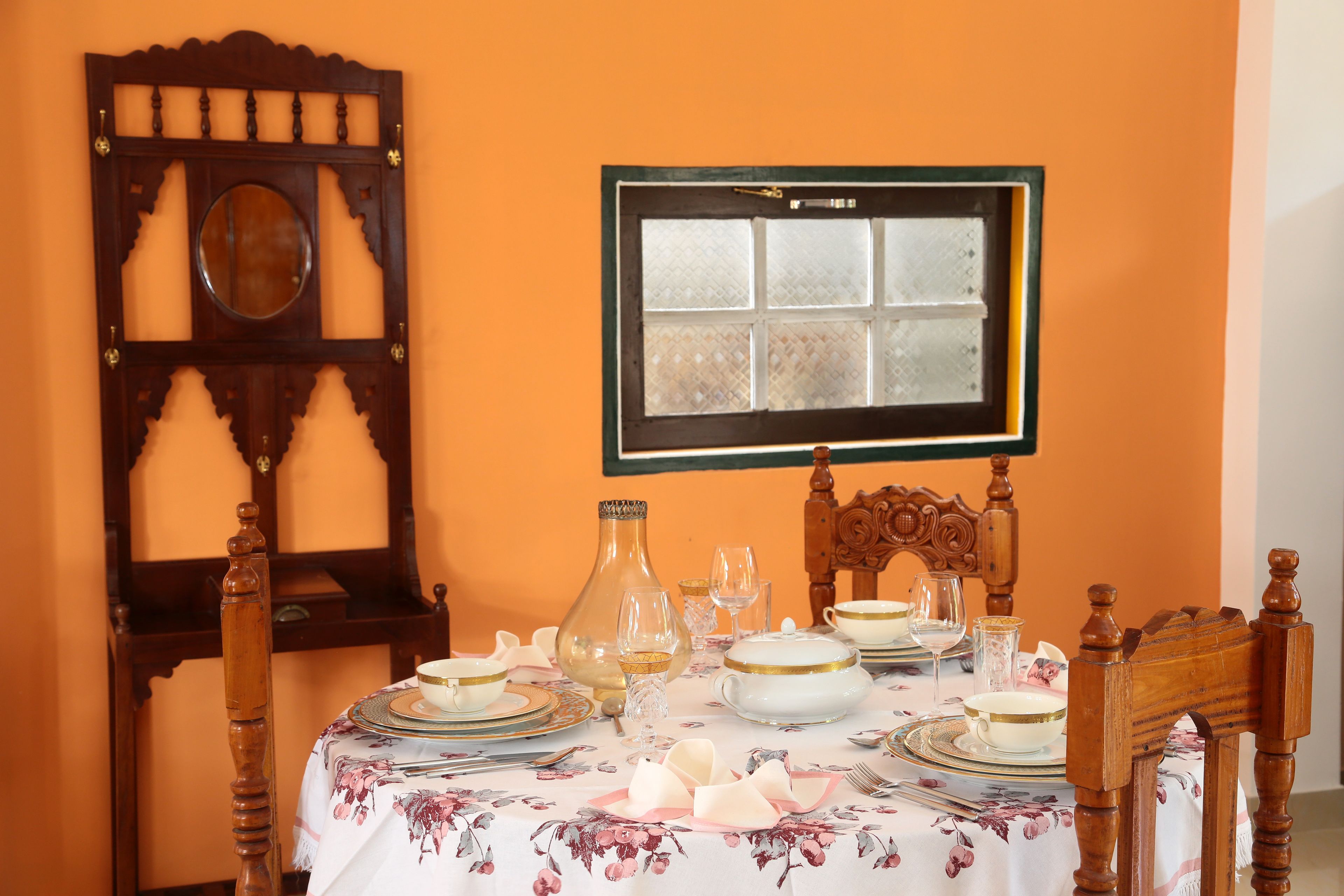 A dining table set with white and gold dinnerware, a vase, and a wooden chair with a carved backrest.