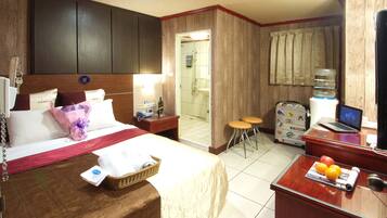 A hotel room with a bed, bedside table, lamp, desk with a laptop, and a bathroom visible through an open door.