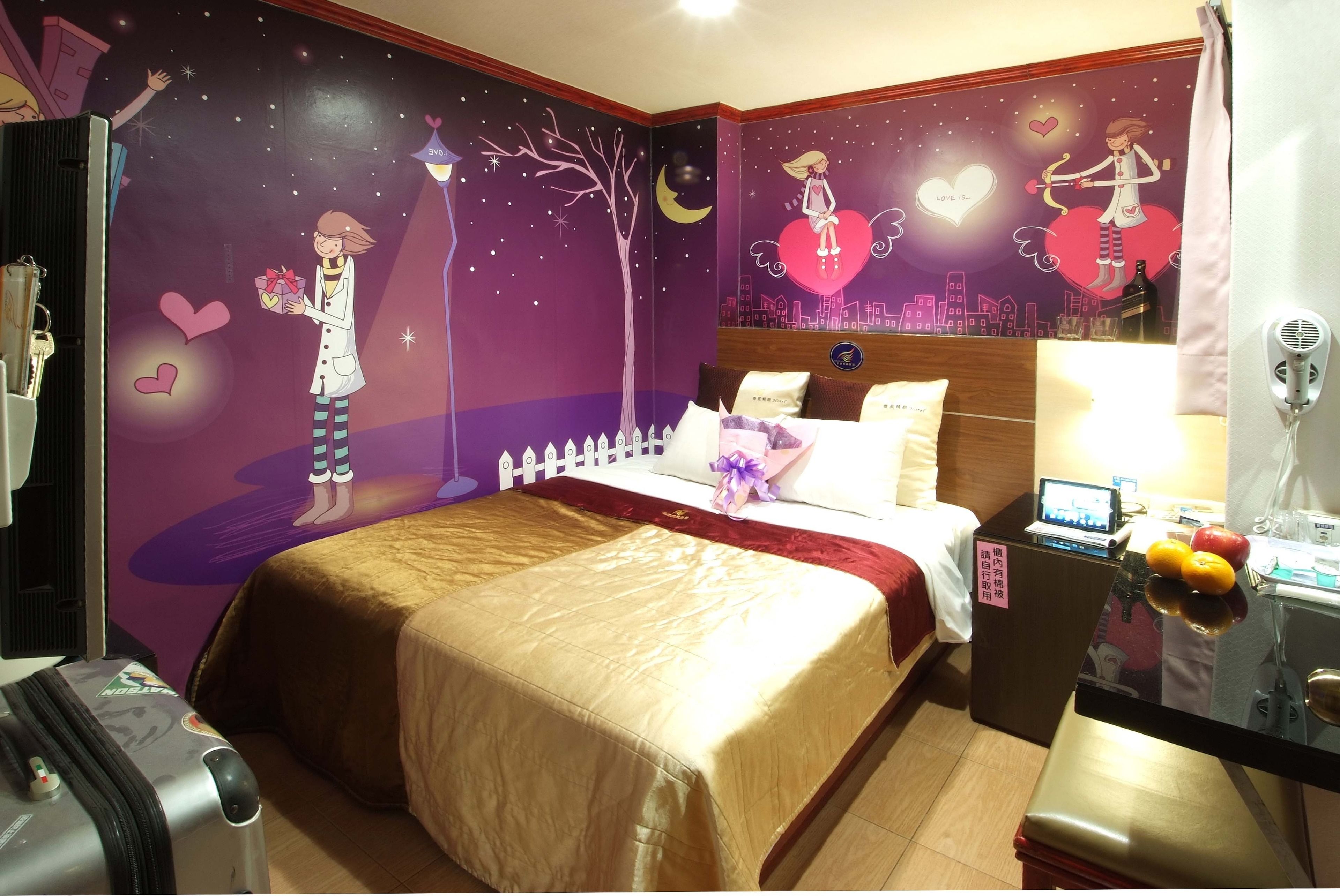 A hotel room with a bed, a desk, and a nightstand. There is a wall mural with a girl holding a gift and a tree.
