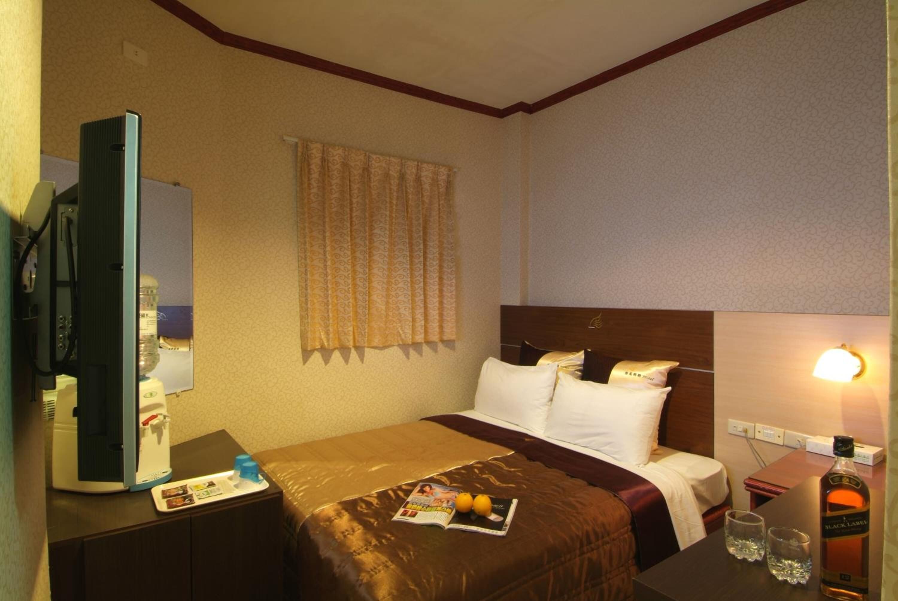 Een hotelkamer met een bed, nachtkastje, lamp en een minibar.