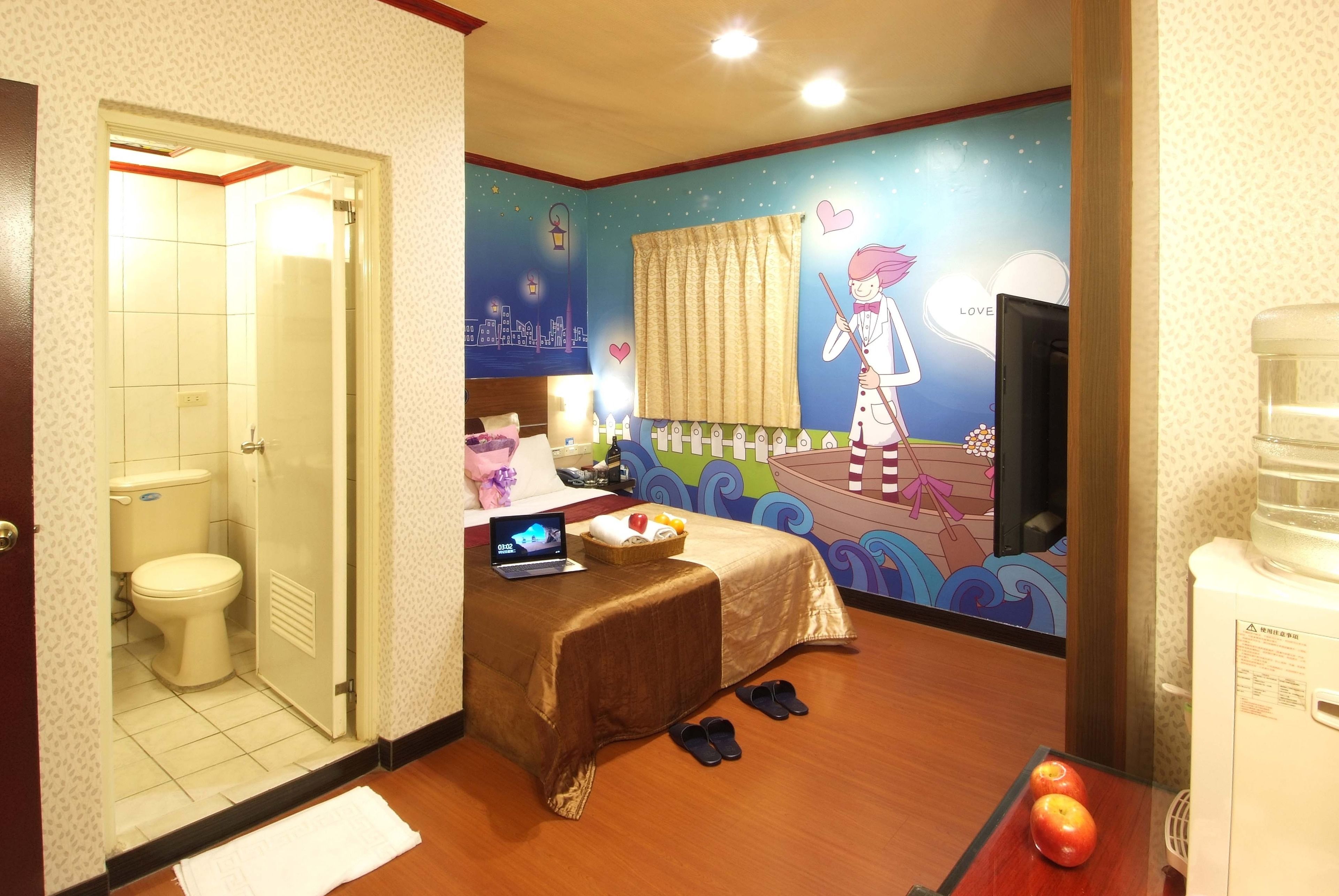 Une chambre d’hôtel équipée d’un lit, d’un ordinateur portable, de chaussons, d’un panier de fruits et d’un distributeur d’eau.
