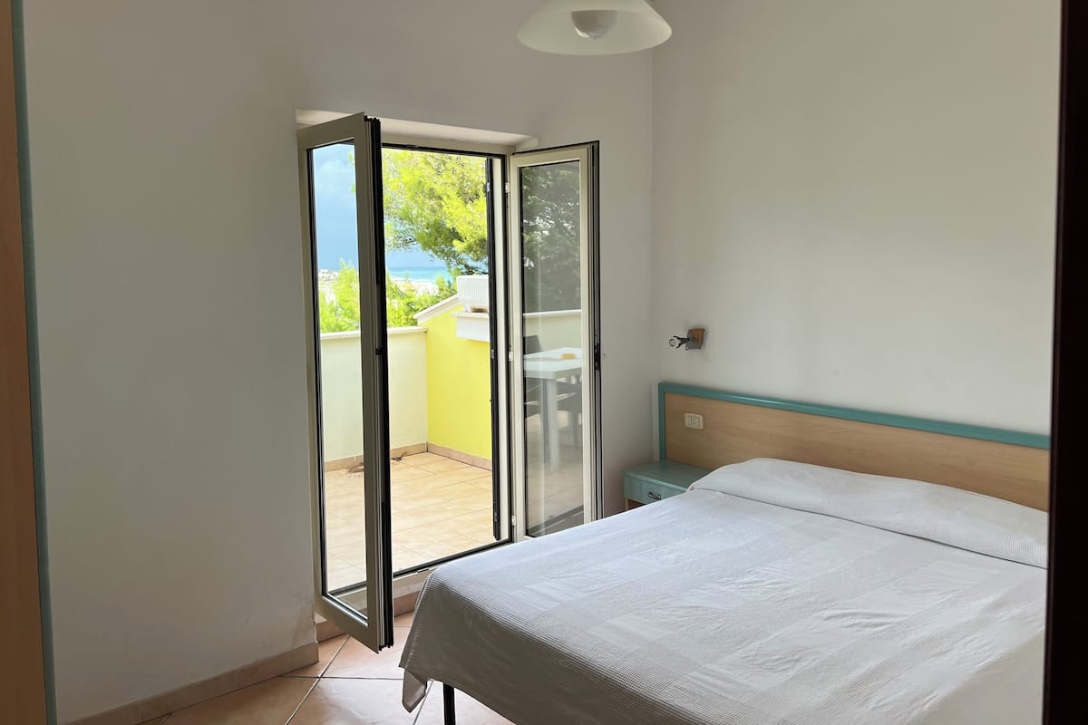 A bedroom with a bed, a nightstand, and a sliding glass door leading to an outdoor area.