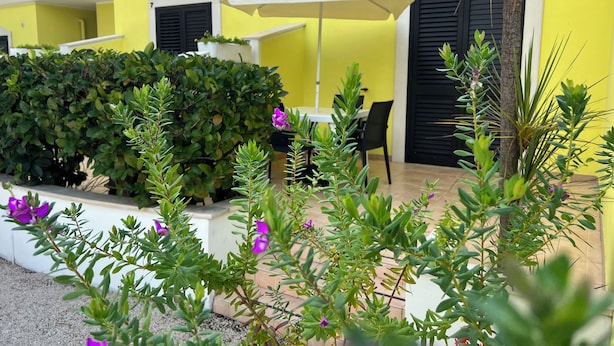 A yellow building with black shutters, a white umbrella, and a table with chairs. - Argeste Club Vacanze (Vieste)