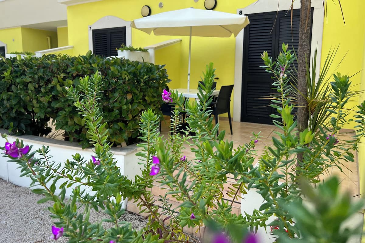 A yellow building with black shutters, a white umbrella, and a table with chairs.