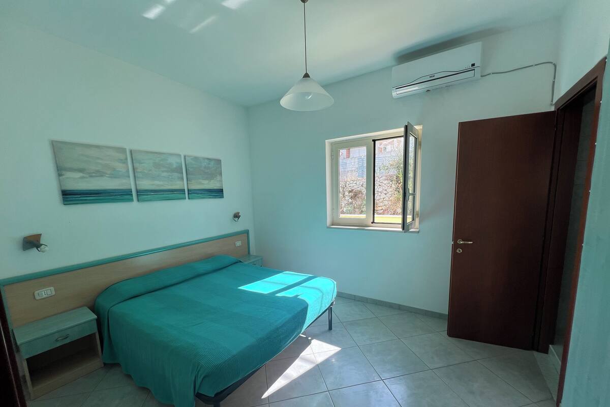 A bedroom with a bed, a nightstand, a window, and a door.