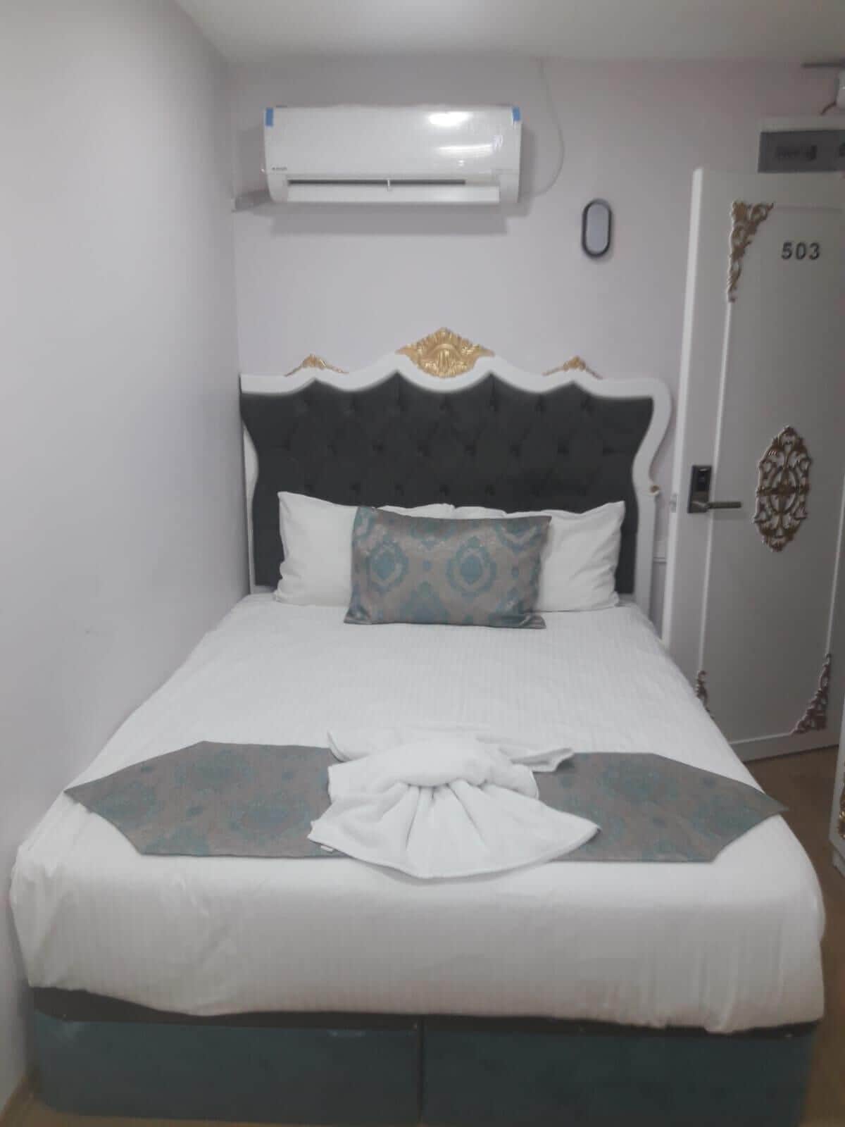 Una cama bien hecha con una colcha blanca y azul, un cojín decorativo y un paño blanco doblado sobre la cama.