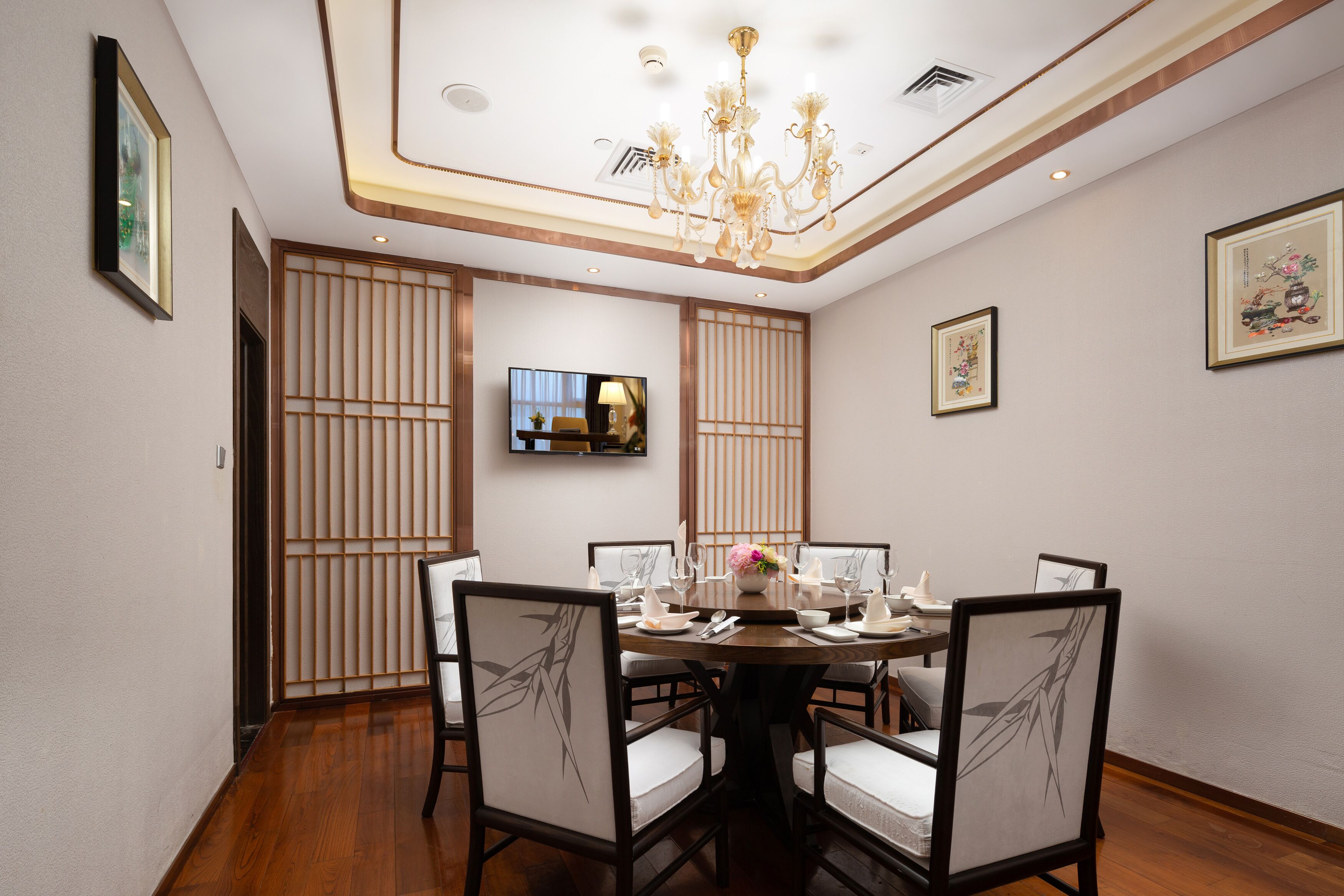 Un comedor con una mesa redonda, sillas, una araña, un televisor y decoración tradicional.