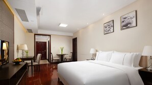 A hotel room with a large bed, a desk with a lamp, a chair, and a small table with a vase of flowers.