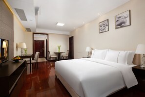 A hotel room with a large bed, a desk with a lamp, a chair, and a small table with a vase of flowers. - Hisoar Hotel Shenzhen (Shenzhen)