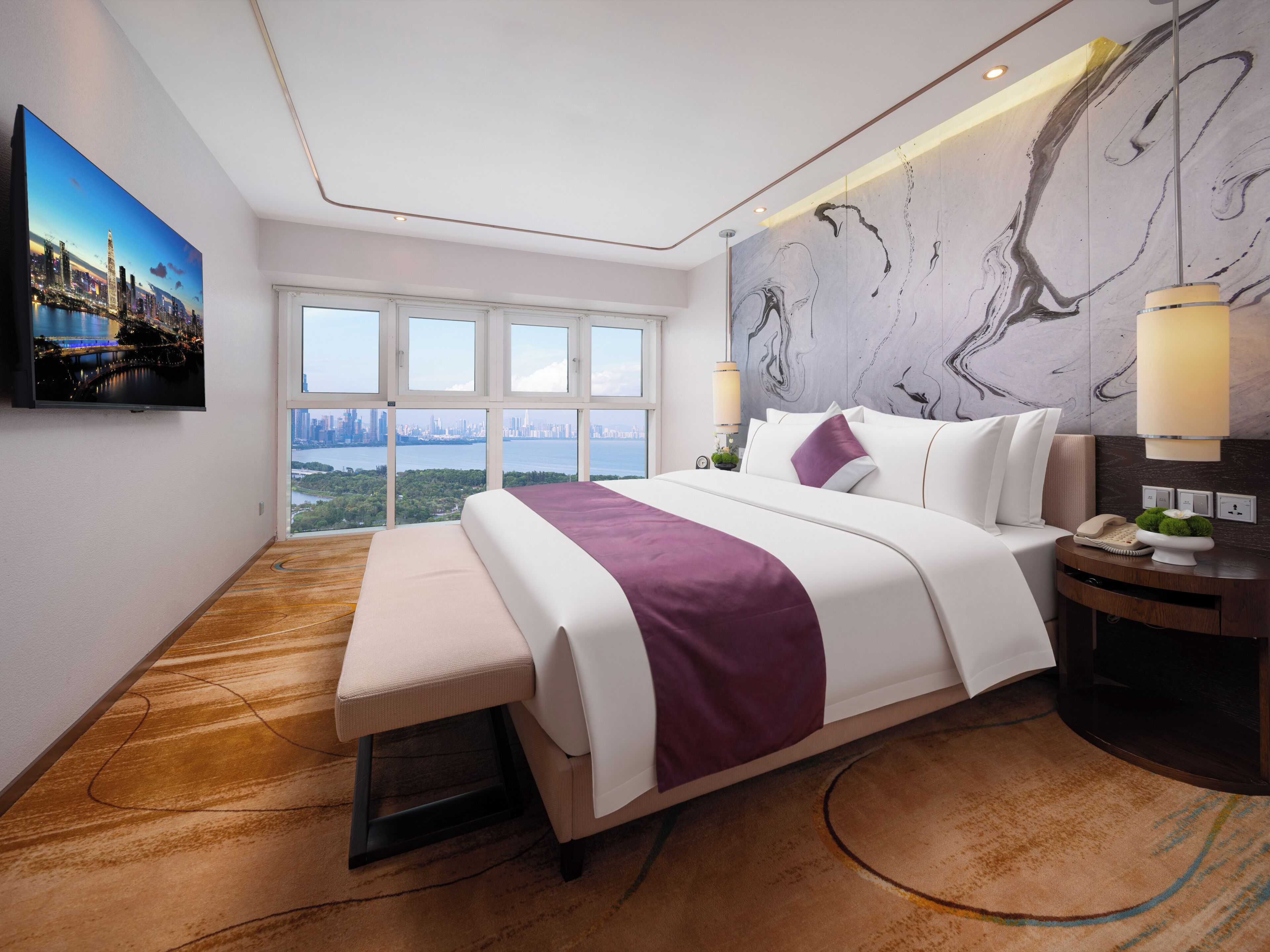 A modern hotel room with a large bed, a city view, a television, and a marble wall.