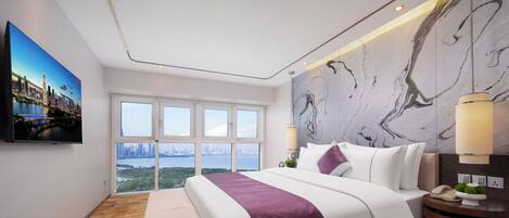 A modern hotel room with a large bed, a city view, a television, and a marble wall.