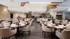 A spacious dining area with multiple tables and chairs, a central column, and a modern ceiling design.