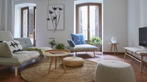 Una sala de estar moderna con un sofá, un sillón, un reposapiés y una mesita con un libro y una planta.