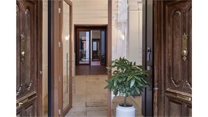 Un pasillo con puertas de madera, una planta en maceta y una vista a una habitación con piso de baldosas y una puerta.