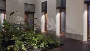 Un edificio moderno con amplios ventanales, una puerta de madera y un jardín con diversas plantas.