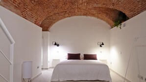 Un dormitorio con una cama blanca, dos lámparas fijadas a la pared y una alfombra roja estampada.