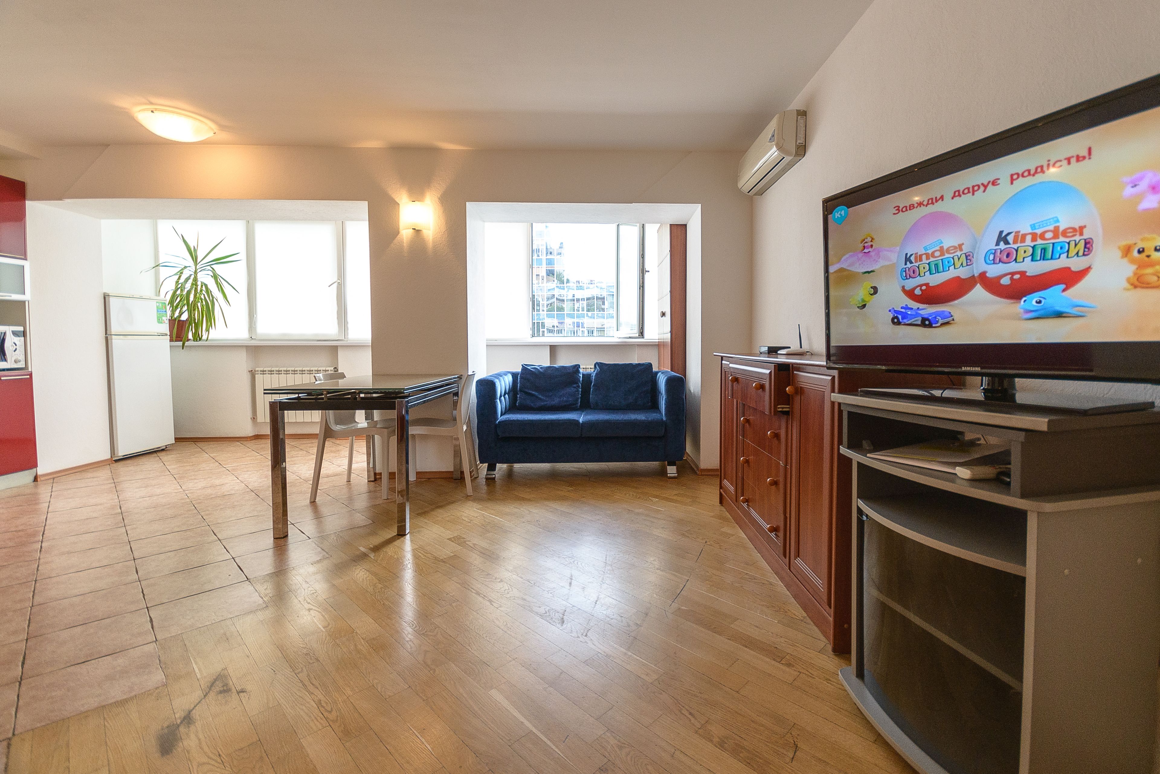 Ein modernes Wohnzimmer mit einer Couch, einem Fernseher, der Kinder Schokolade zeigt, einem Esstisch und einer Zimmerpflanze.