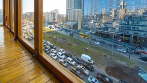 A view from a window overlooking a busy urban street with tall buildings, parked cars, and a yellow bus. - Partner Guest House (Kyiv)