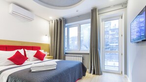 Ett modernt hotellrum med en stor säng, grå gardiner, utsikt över staden och en väggmonterad TV.