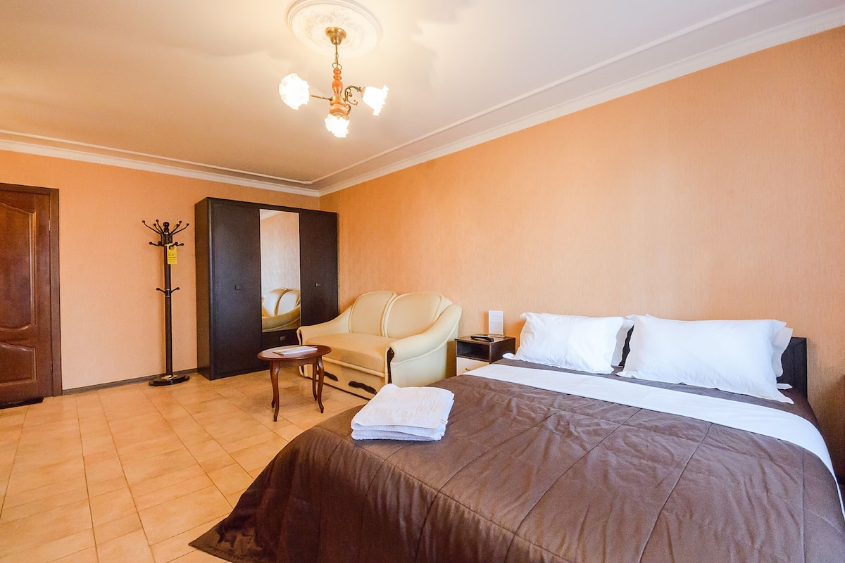 A hotel room with a large bed, a chair, a nightstand, a lamp, and a coat rack.