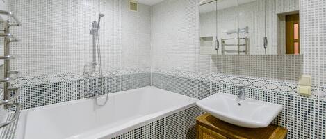 Un baño con una bañera blanca, un lavamanos y un espejo sobre él.