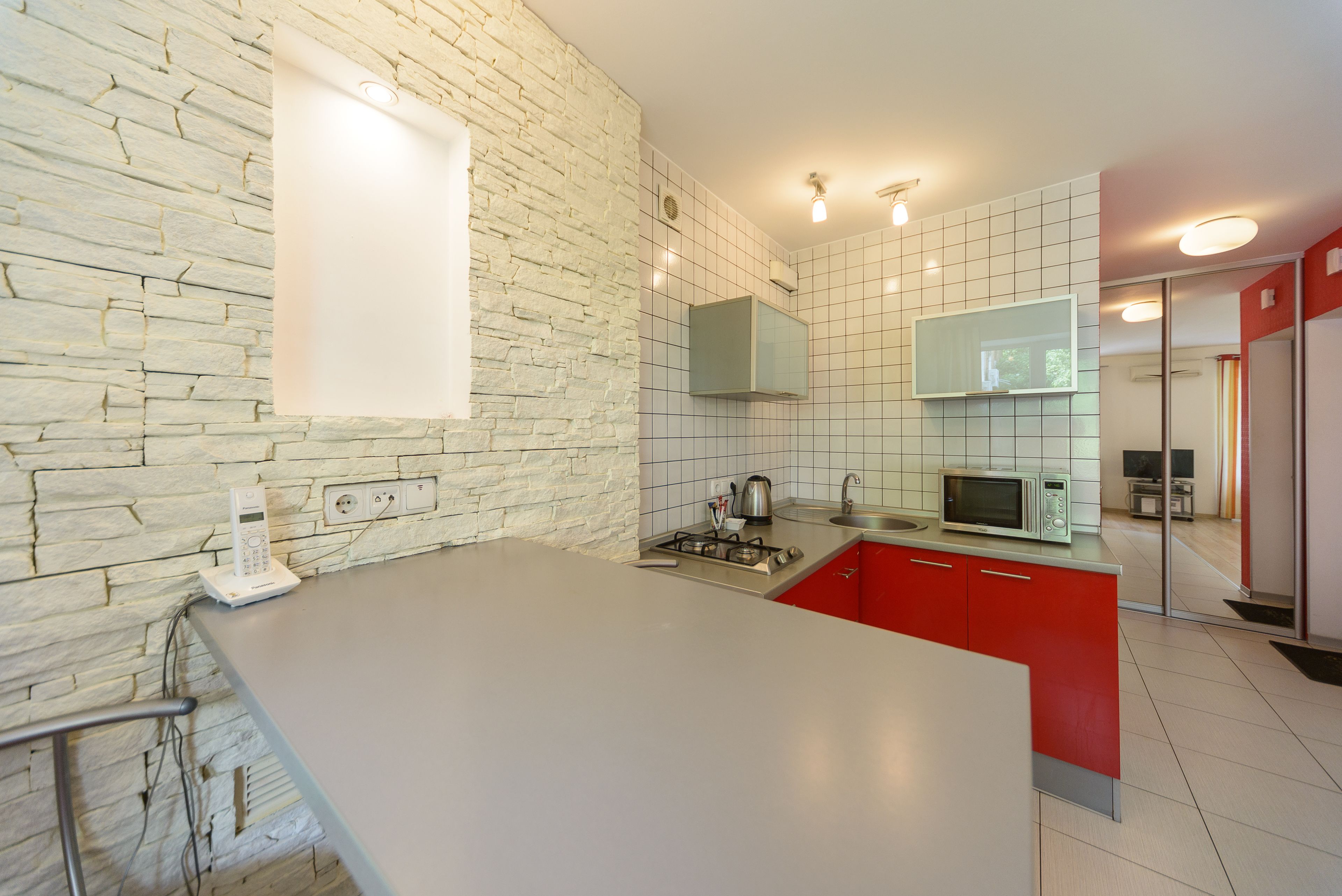 Una cocina moderna con pared de piedra, armarios rojos y una isla grande.