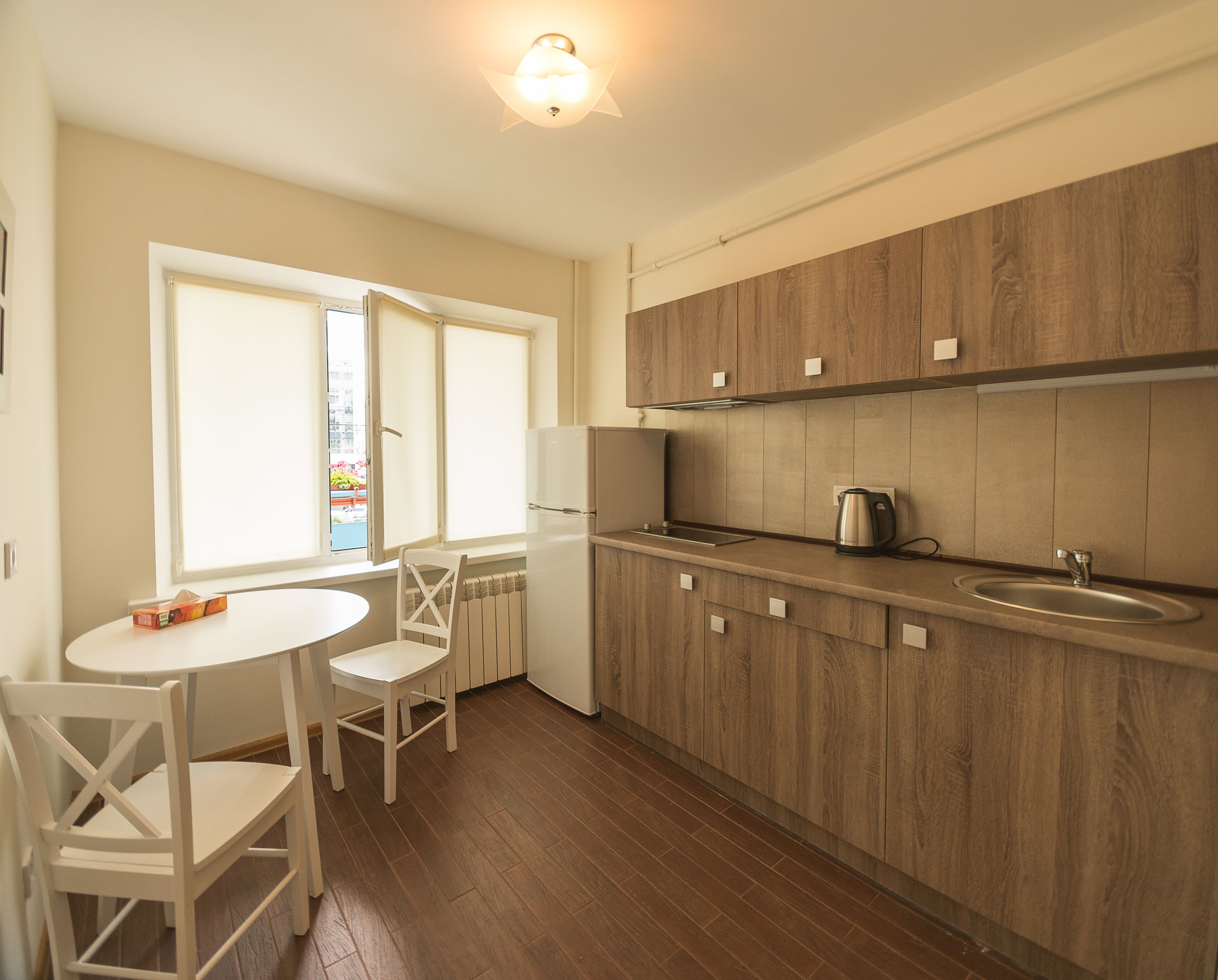 A kitchen with wooden cabinets, a white refrigerator, a kettle, and a window with a view of the outside.