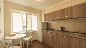 A kitchen with wooden cabinets, a white refrigerator, a kettle, and a window with a view of the outside.