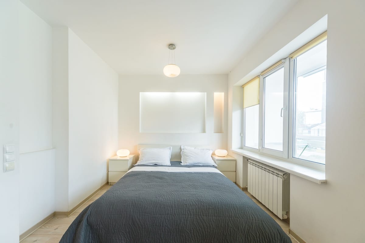 A bedroom with a bed, bedside lamps, a window, and a radiator.