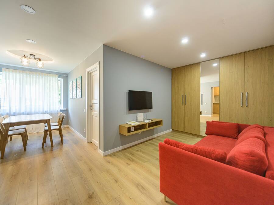 Una sala de estar moderna con un sofá rojo, una mesa de comedor de madera y un televisor montado en la pared.