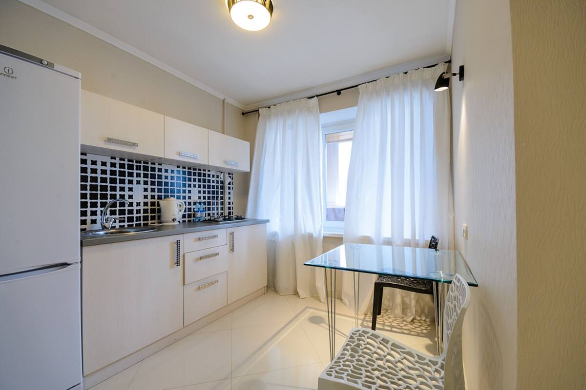 A modern kitchen with white cabinets, a glass-top table, and a white refrigerator.