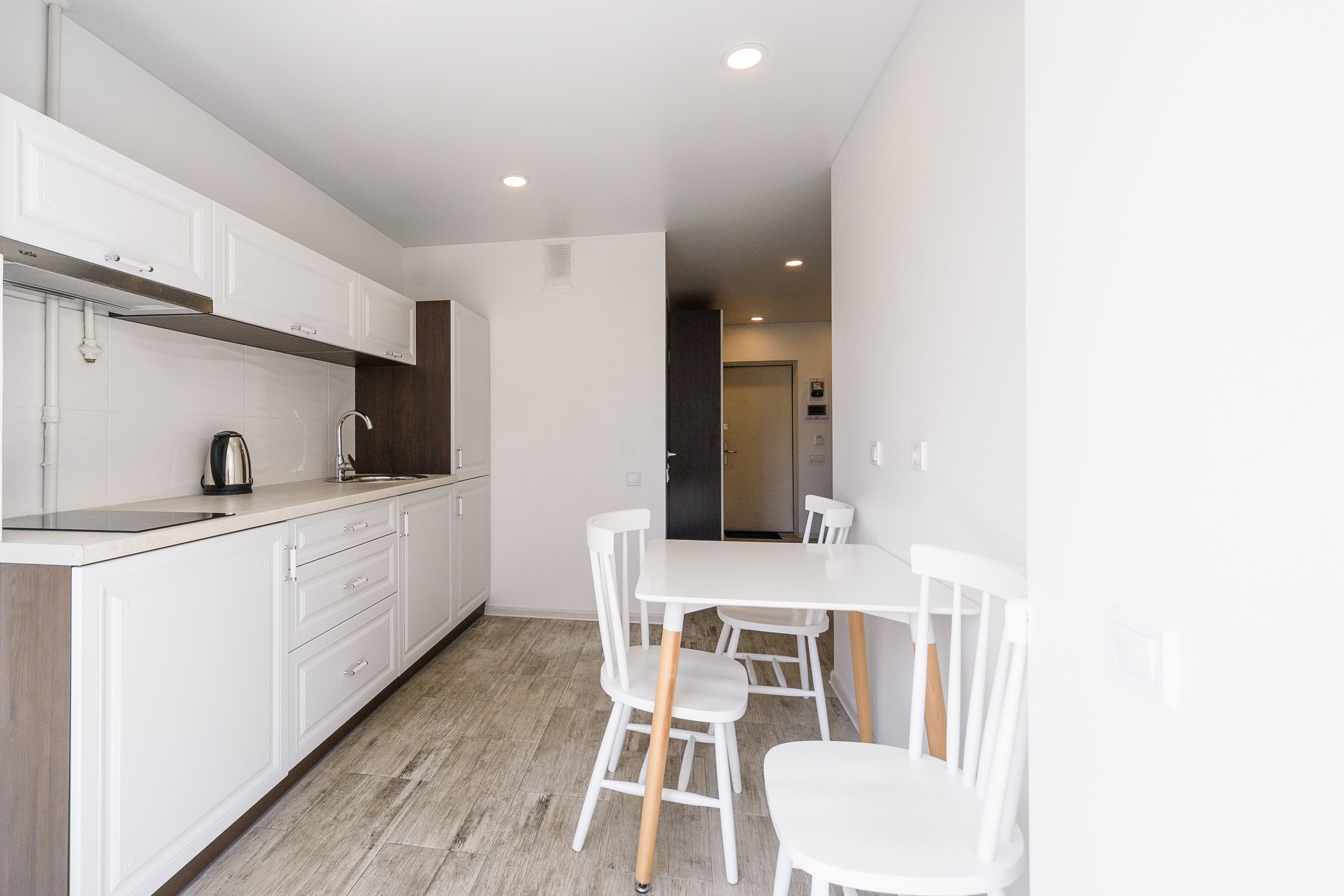 Una cocina moderna con armarios blancos, encimera de madera y un comedor con sillas y mesa blancos.