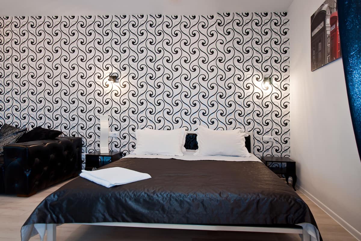 A neatly made bed with a dark brown bedspread, a black headboard, and a patterned wallpaper.