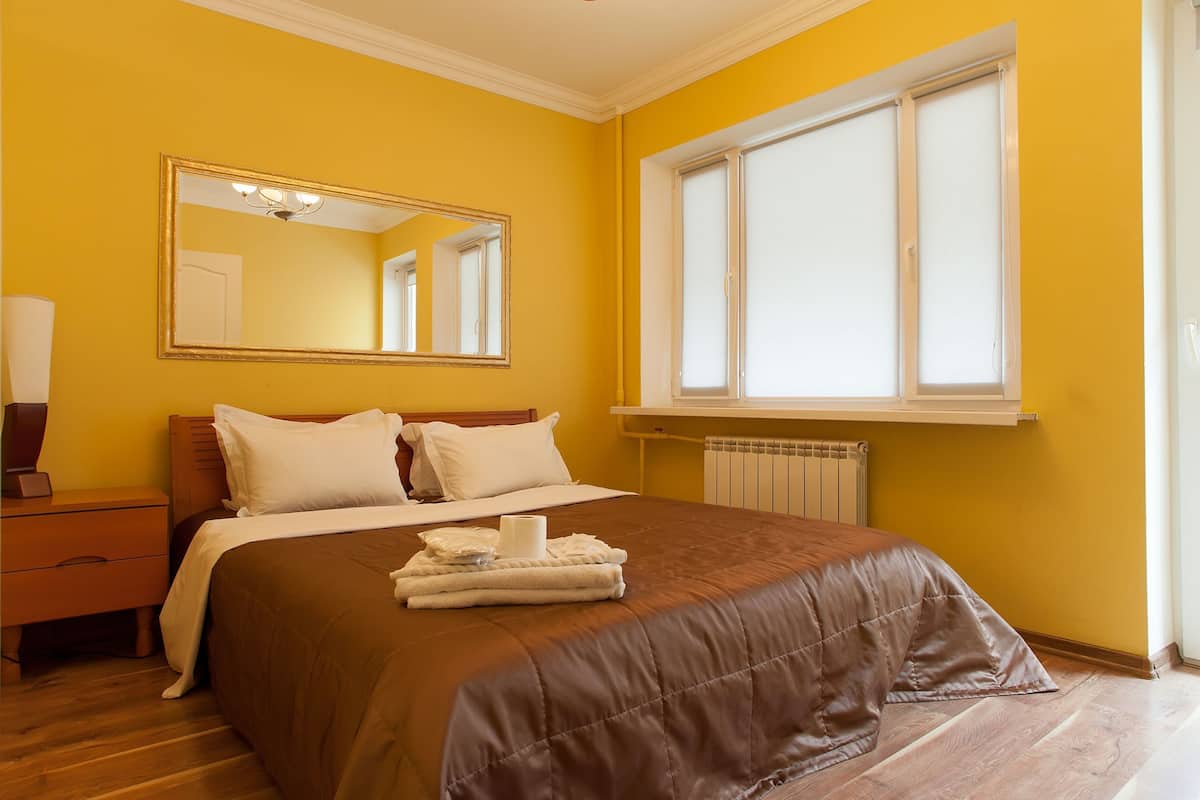 A hotel room with a large bed, a bedside table, a mirror, and a window with blinds.