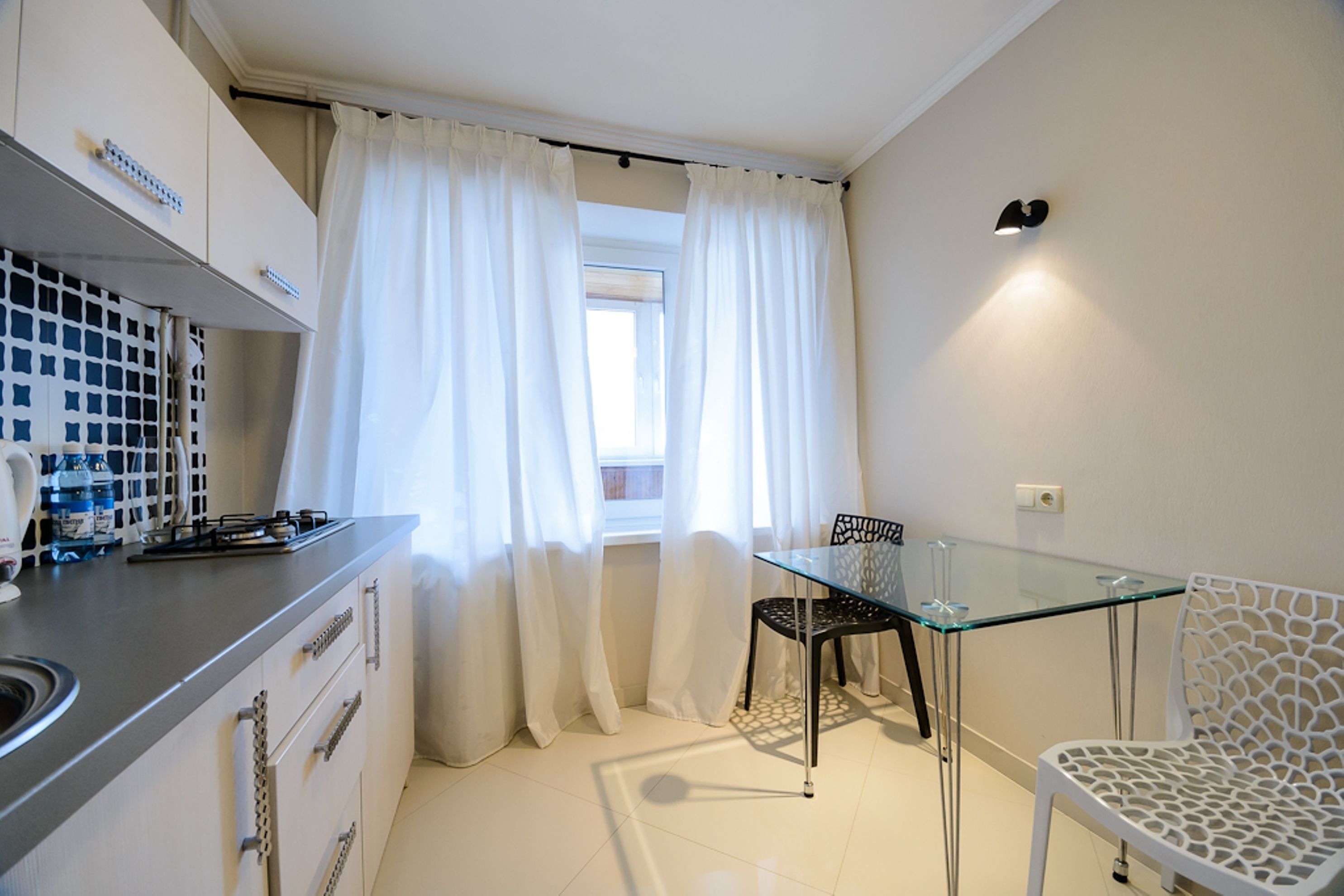 A compact kitchen with a gas stove, white cabinets, and a window with sheer curtains.