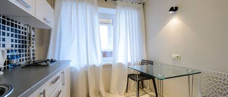 A compact kitchen with a gas stove, white cabinets, and a window with sheer curtains.