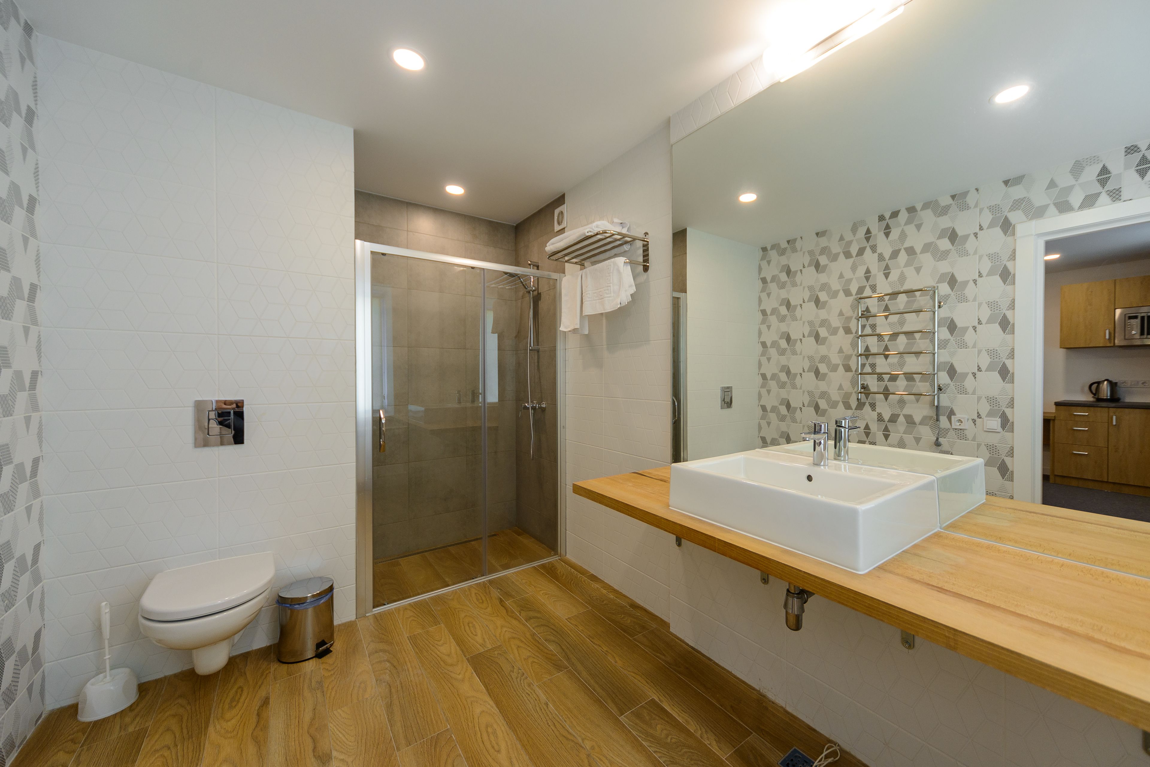 A modern bathroom with a large mirror, a wooden vanity, a shower enclosure, and a toilet.