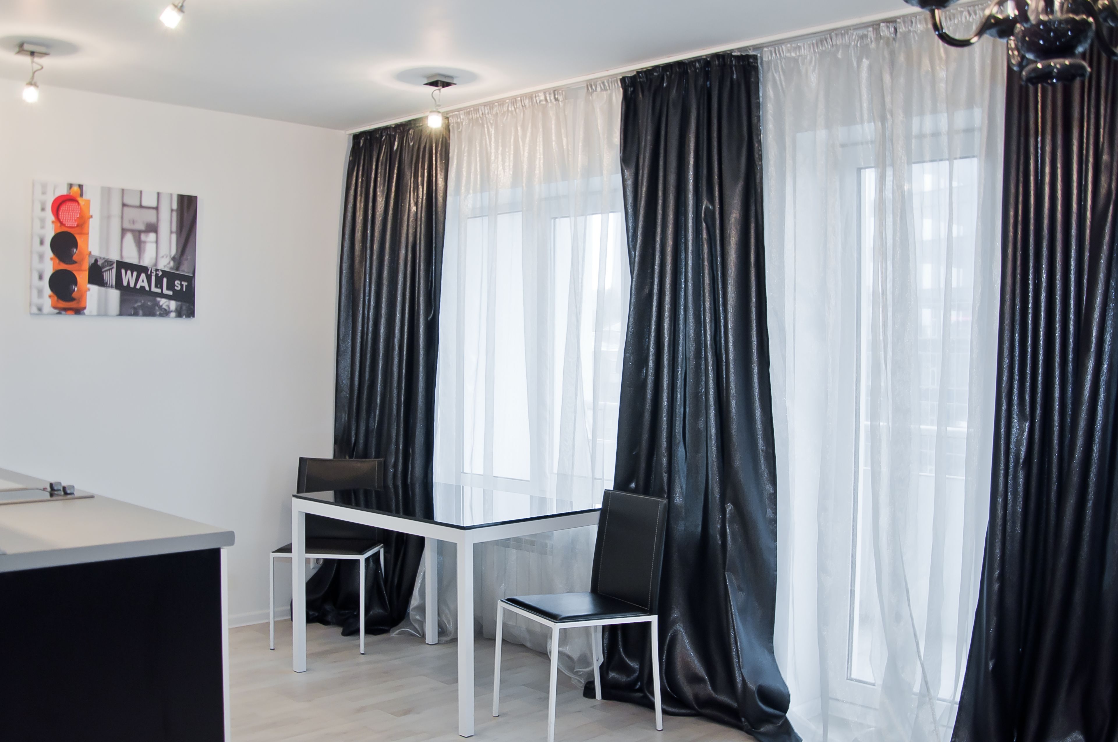 Una habitación moderna con una mesa de cristal, dos sillas, un escritorio y un ventanal con cortinas translúcidas.