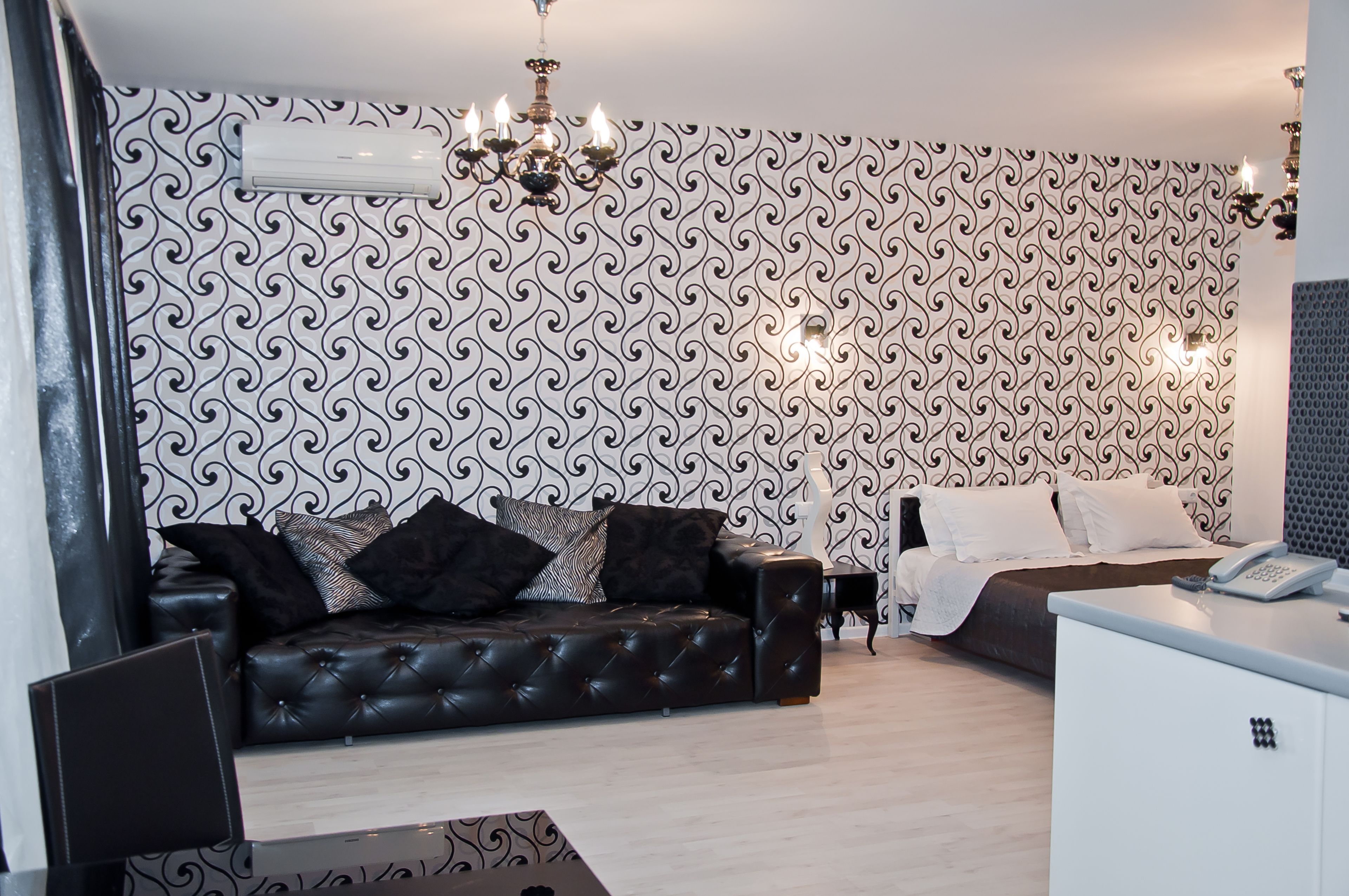 Una sala de estar moderna con un sofá de cuero negro, un escritorio blanco y un papel tapiz estampado.