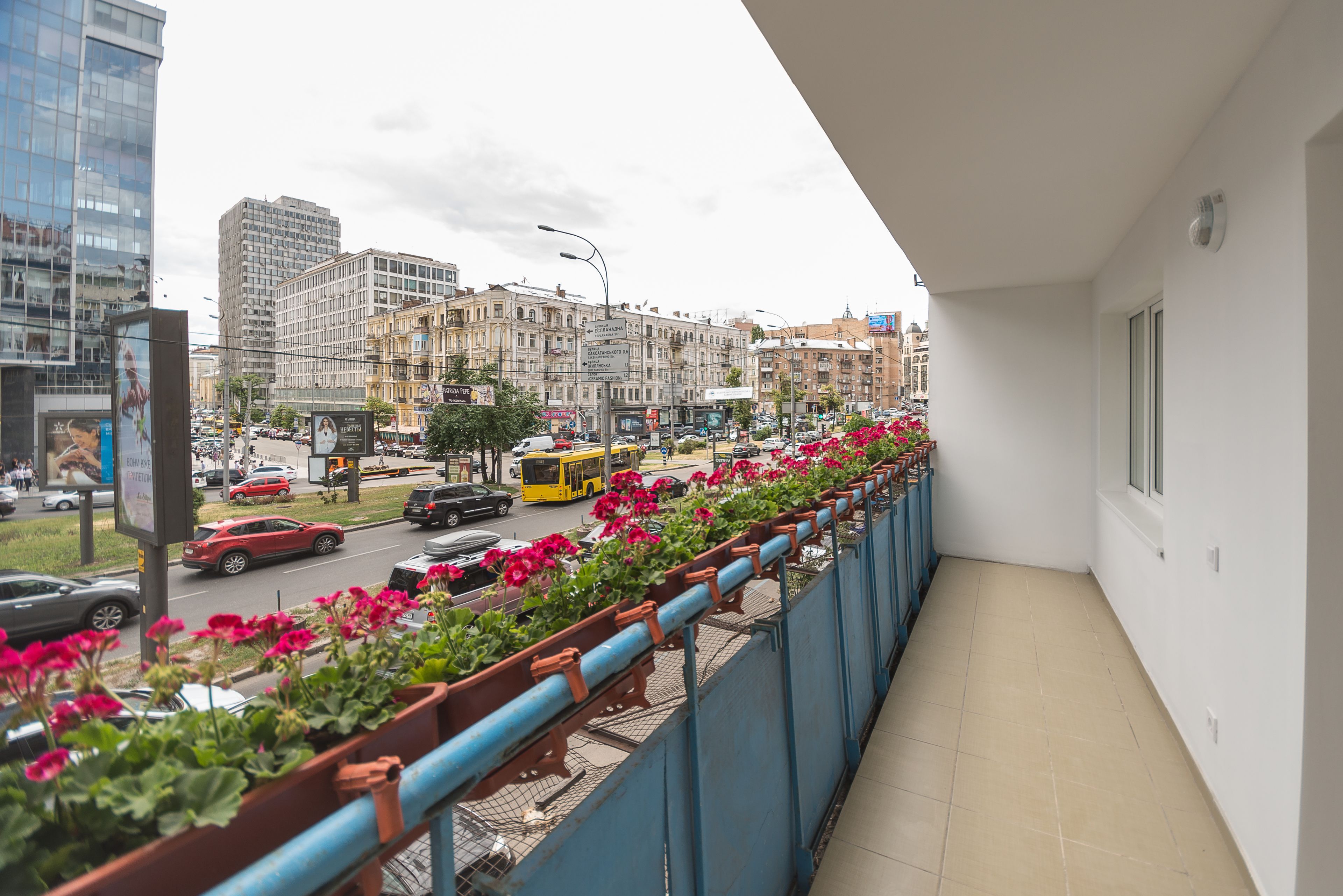 A balcony with a view of a busy street, buildings, and a row of flower pots.