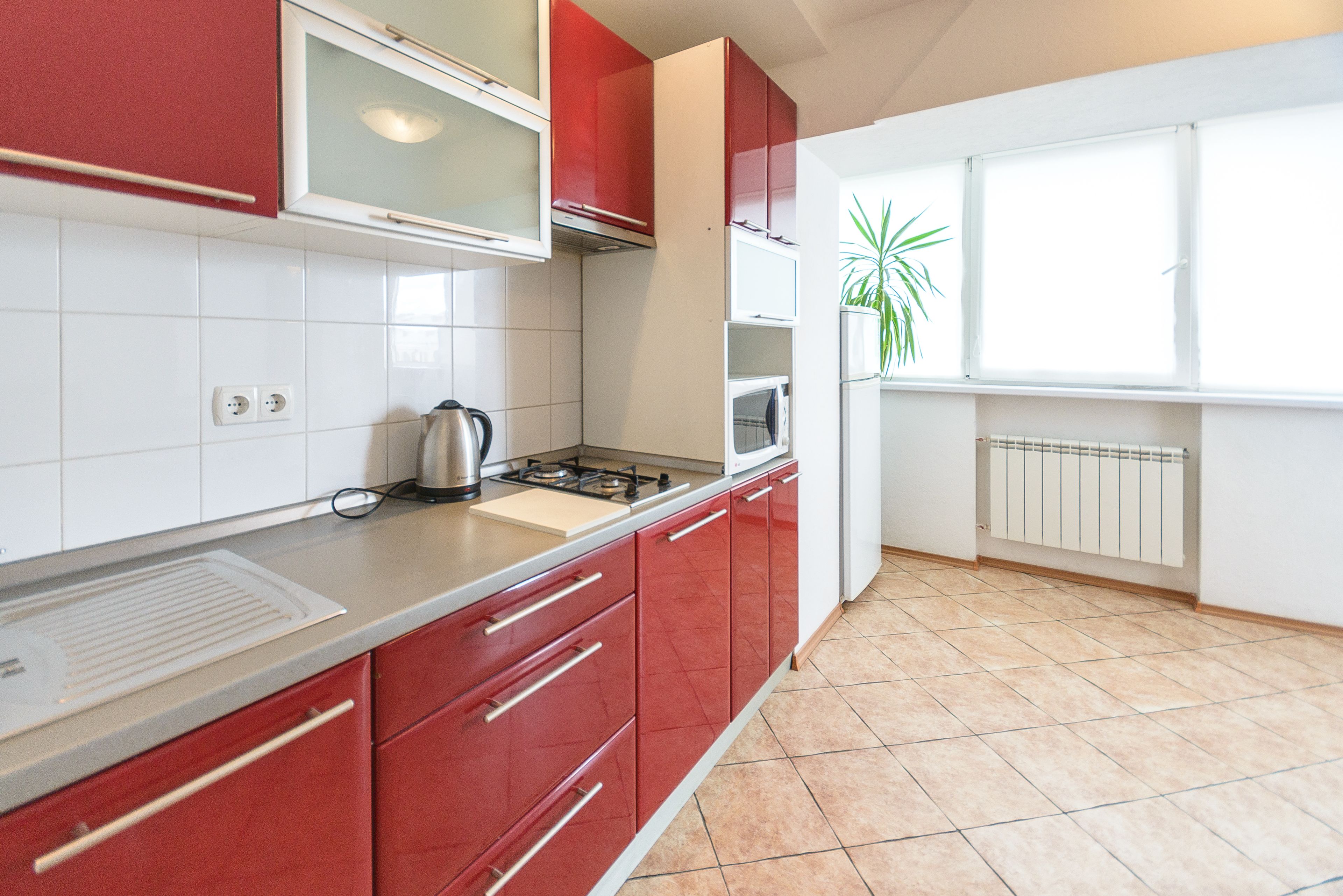 Cucina con mobili rossi, fornello a gas, bollitore e finestra con una pianta.