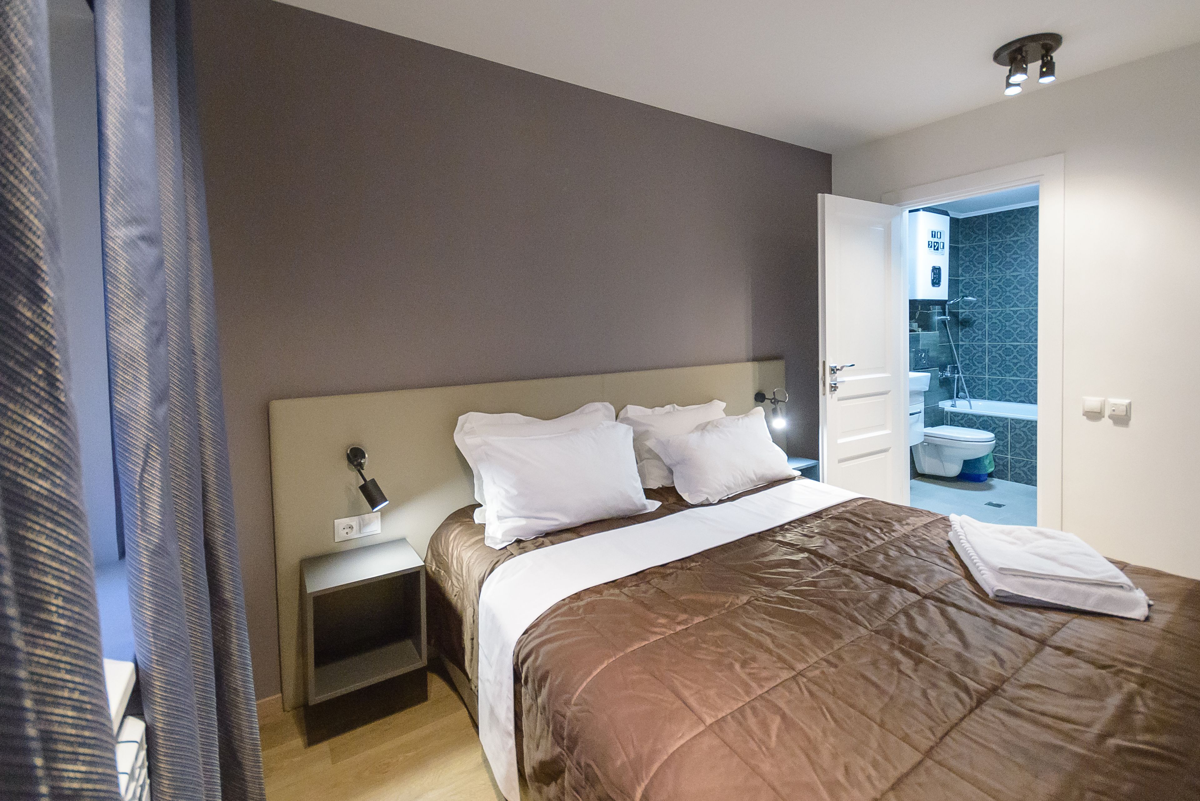 Habitación de hotel moderna con una cama grande, una mesita de noche y un baño visible a través de una puerta abierta.