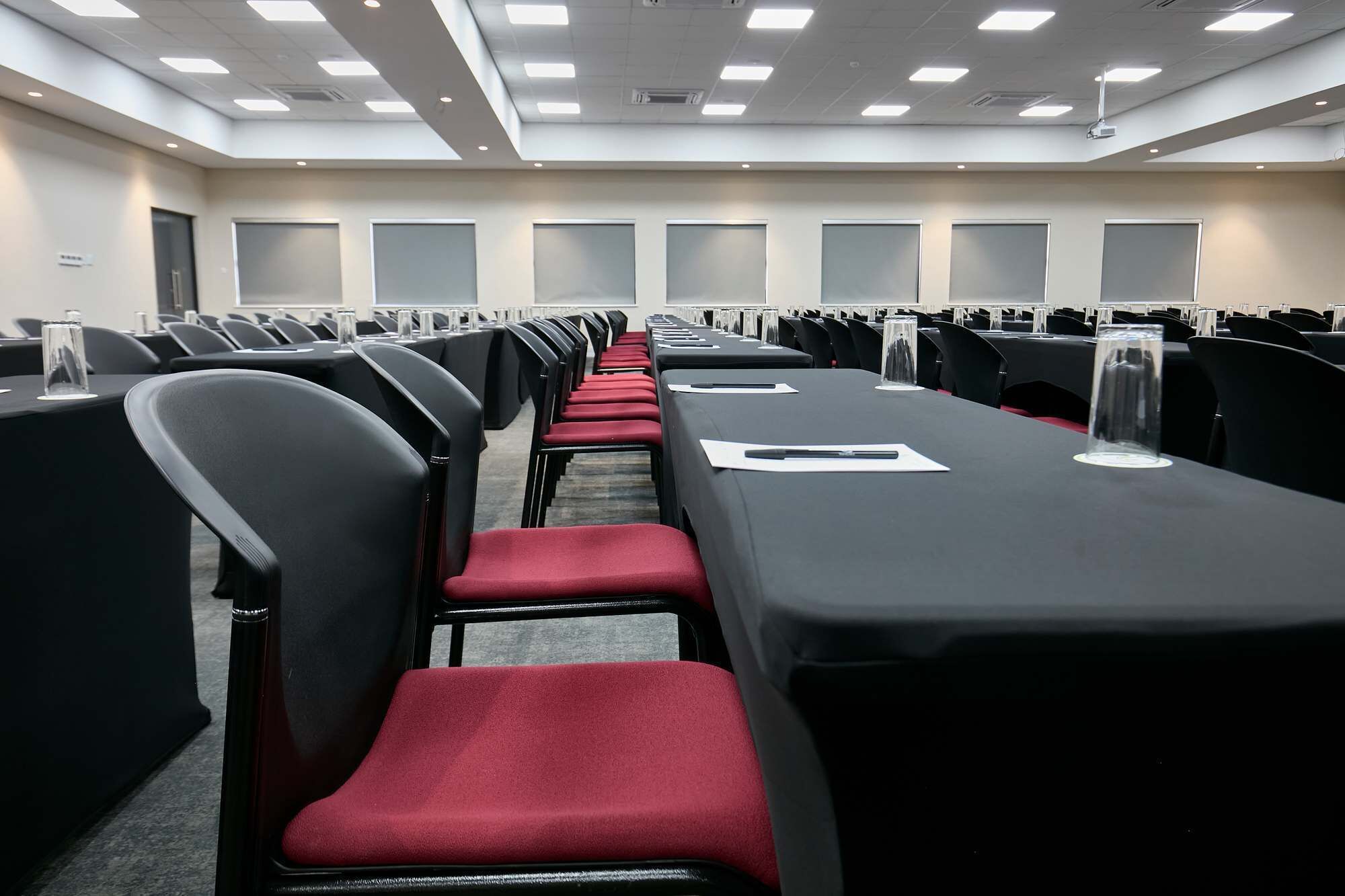 Une salle de conférence avec des rangées de chaises noires et des coussins rouges, une longue table couverte de papiers et de verres, et un écran de projection à l’avant.