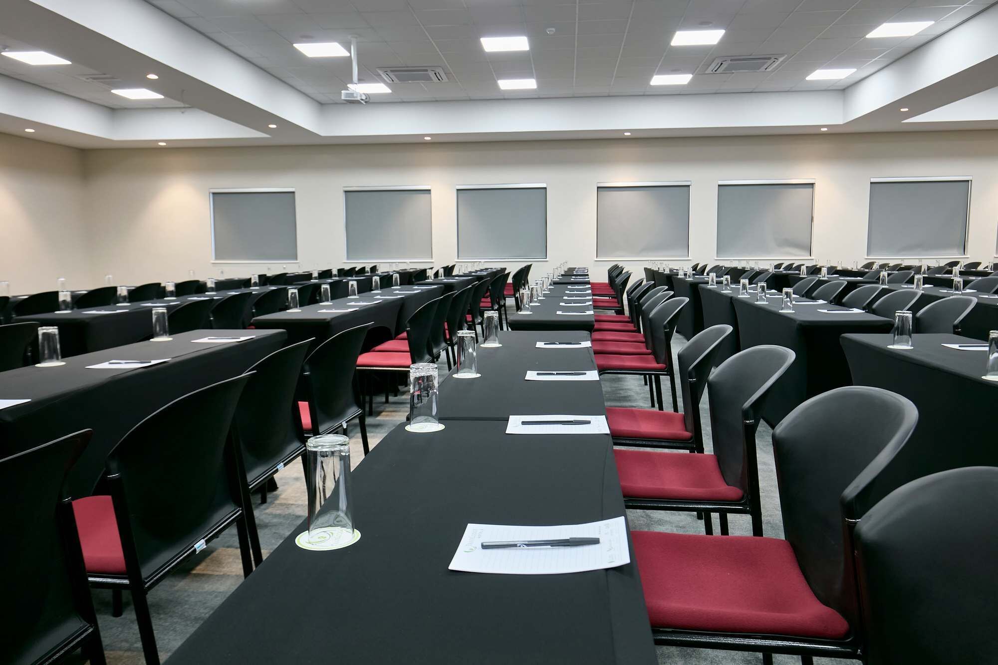 Un salón de conferencias con filas de mesas y sillas, equipado con tarjetas de identificación y vasos de agua.