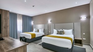A hotel room with two beds, a desk, and a large window with curtains.