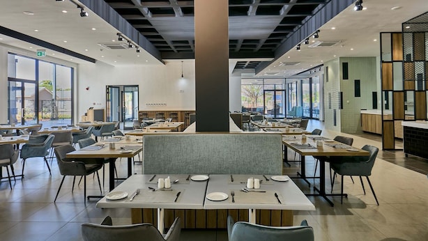 A modern dining area with multiple tables and chairs, large windows, and a central pillar.