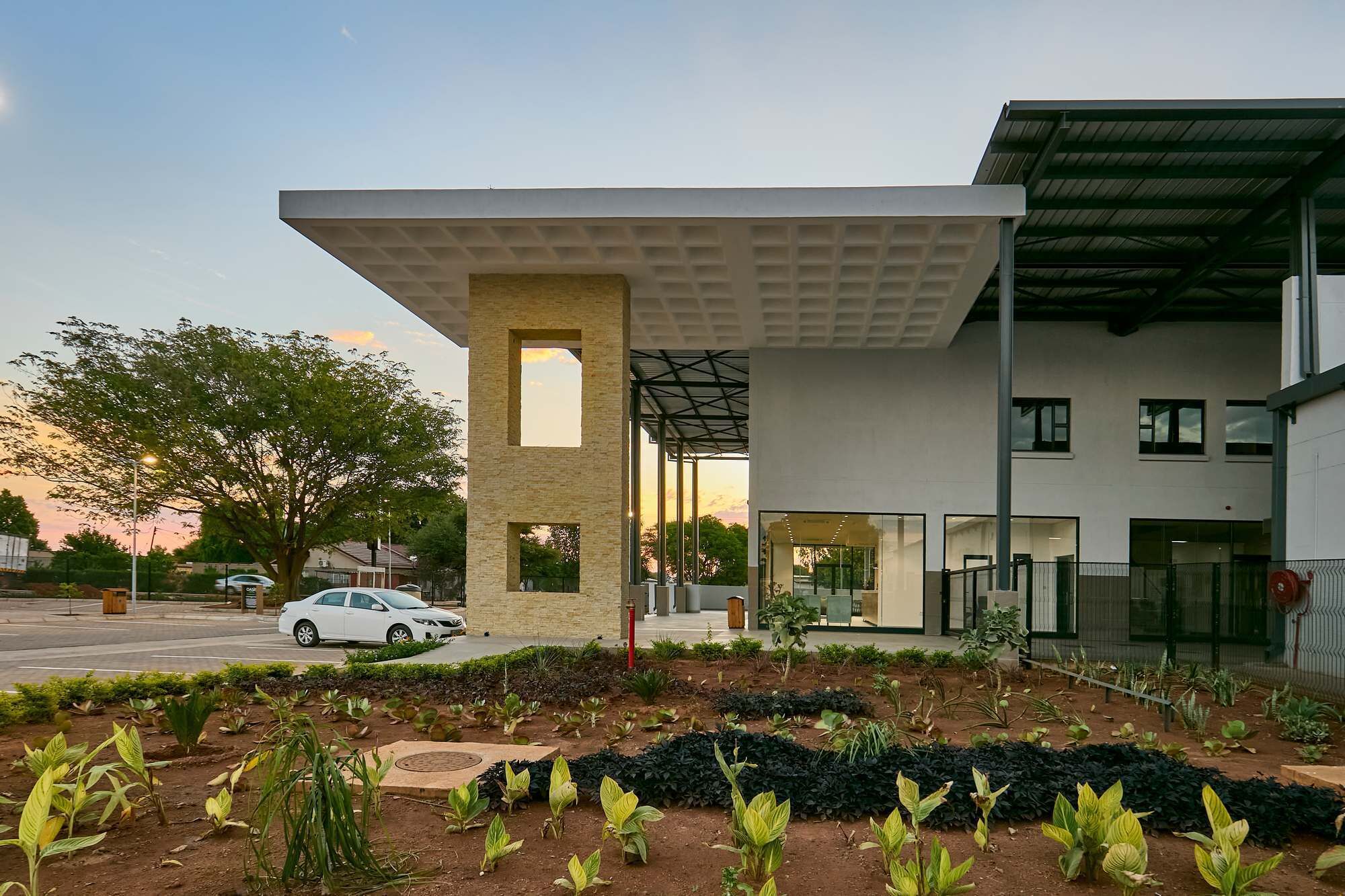 A modern building with a flat roof, large windows, and a covered entrance area with a garden in front.