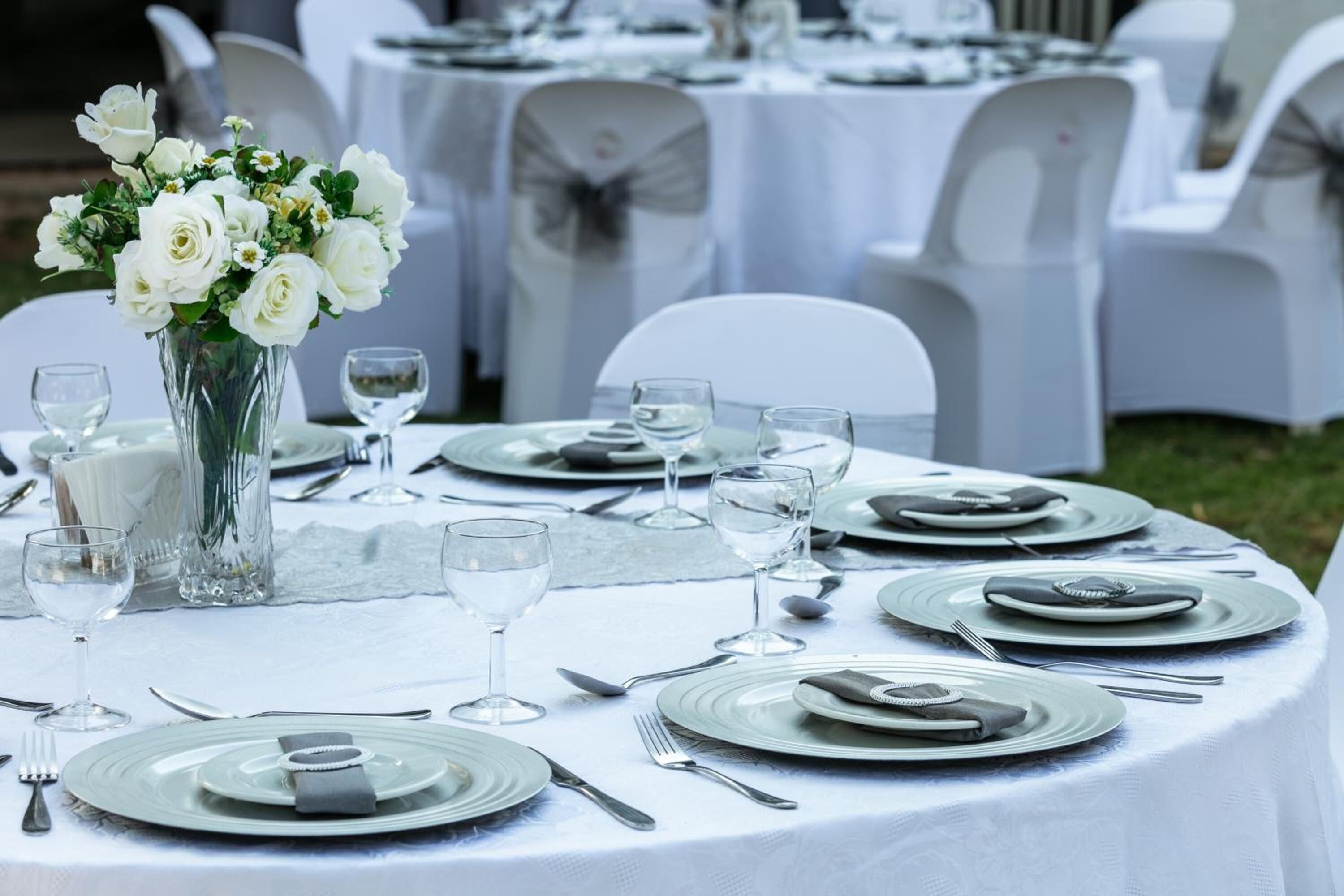 Une table dressée pour un événement formel, avec des nappes blanches, des assiettes, des couverts et un vase rempli de fleurs blanches.