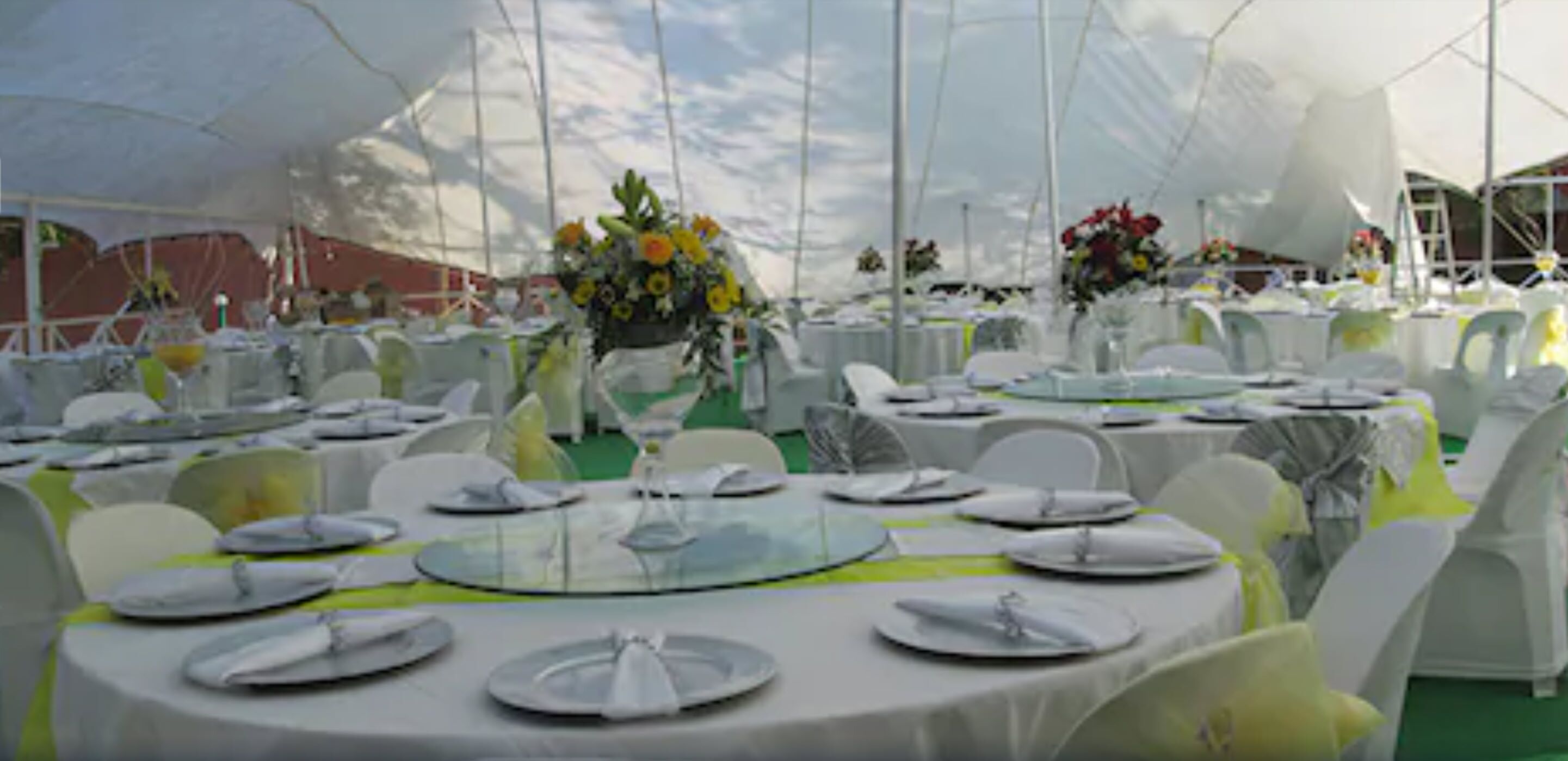 A tented outdoor event space with round tables set for dining, white chairs, and floral centerpieces.