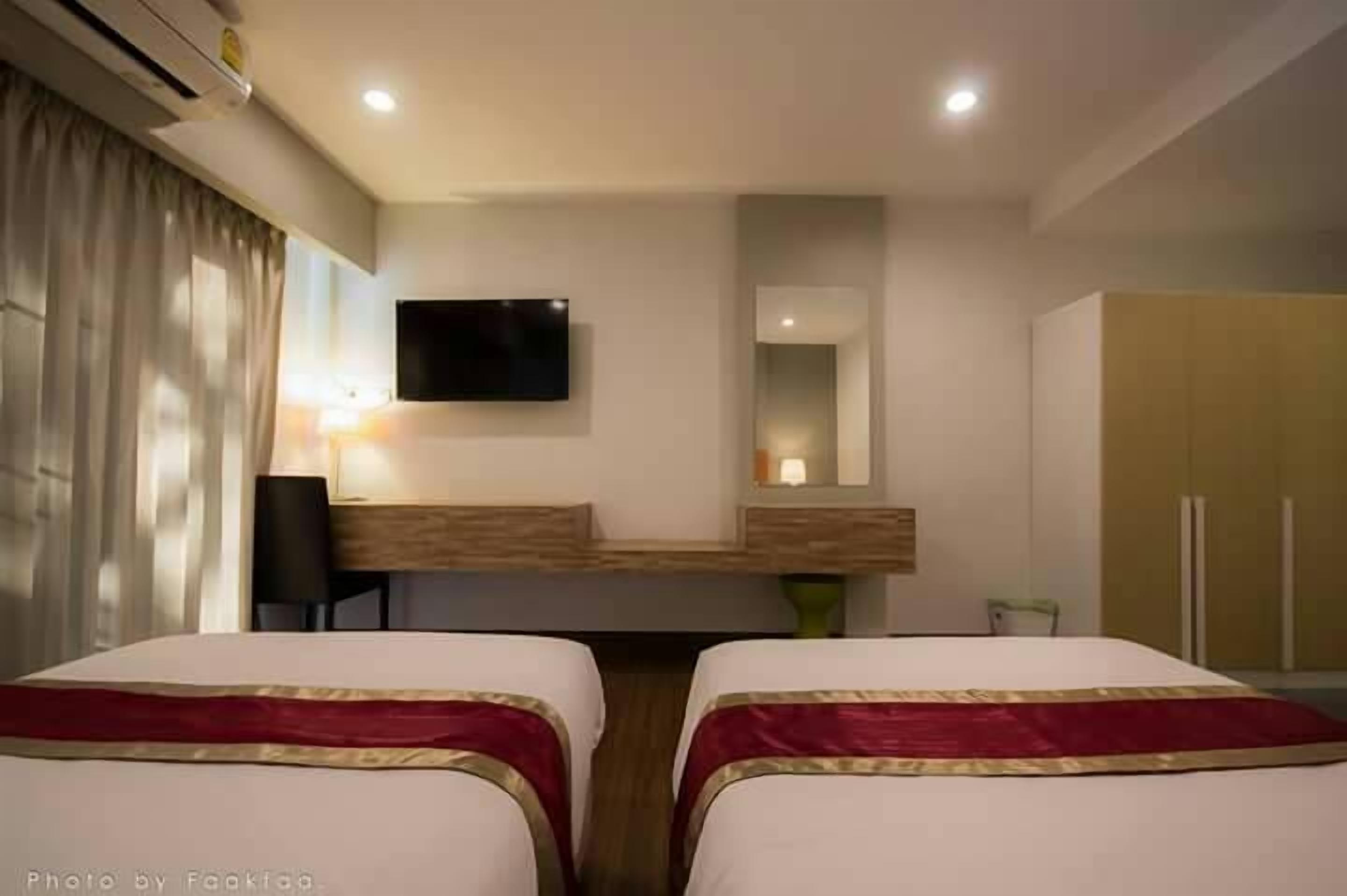 A hotel room with two beds, a TV mounted on the wall, a desk with a chair, and a wardrobe.